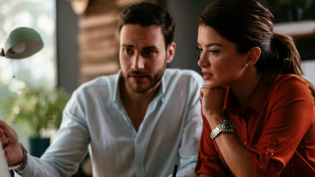 A couple discussing something while using a laptop.