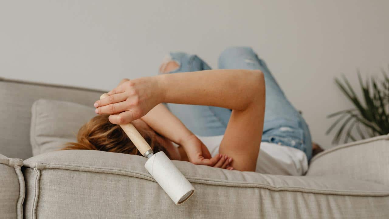 A person lying on a couch holding a lint roller.