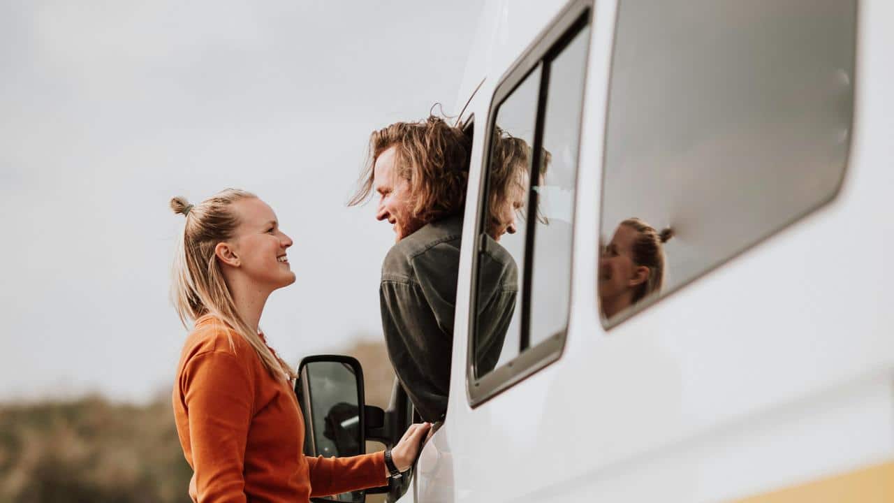 A smiling couple talking beside a white van.