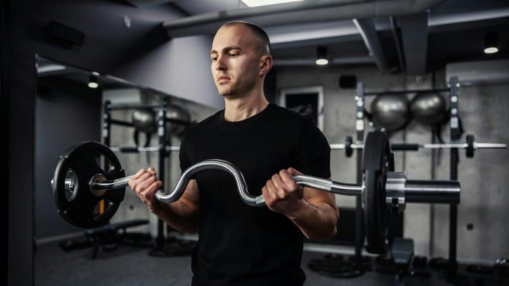 Man in a black t-shirt doing bicep curls with an E-Z curl bar.