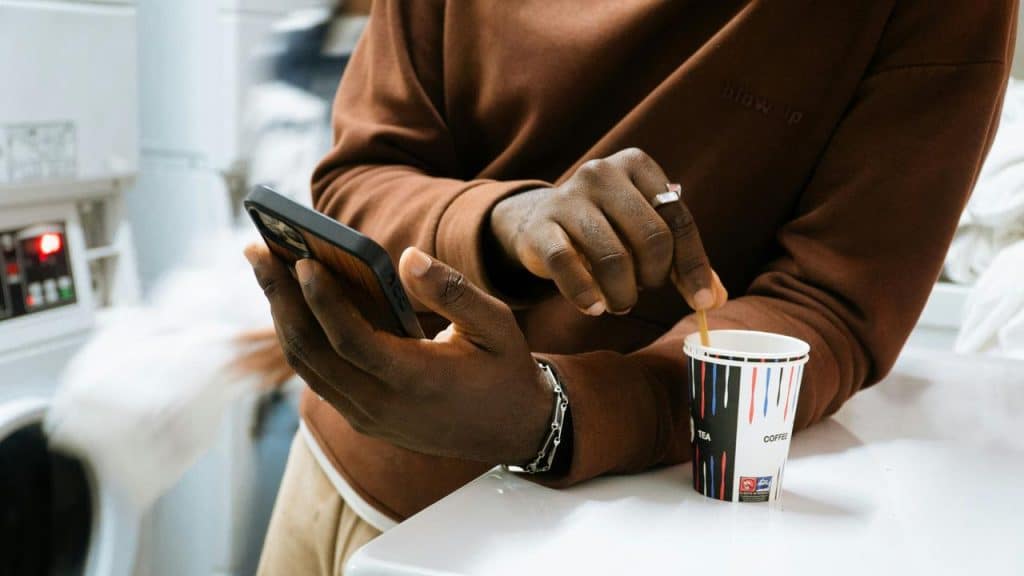 A person stirring coffee while checking a smartphone.