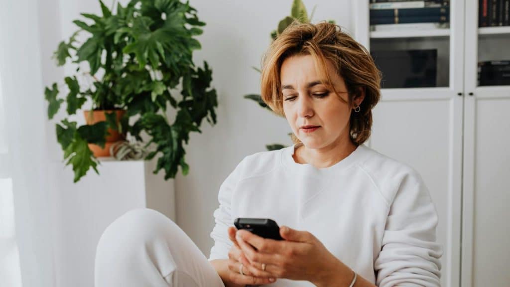 A woman sitting indoors looking at her phone.