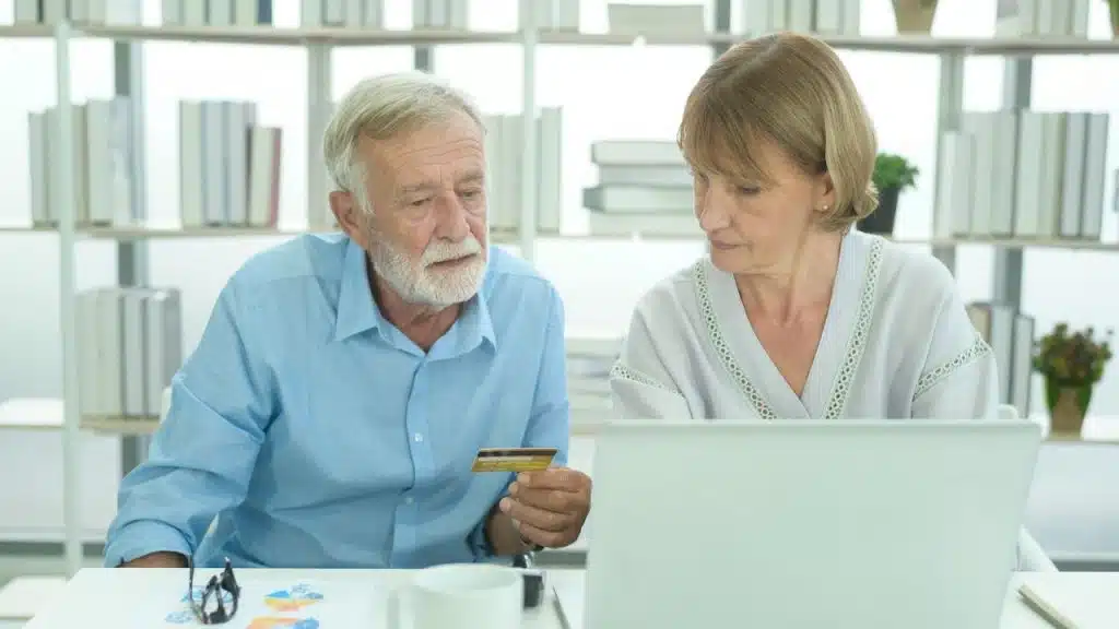 Elderly man holding a credit card and woman looking at a laptop together.