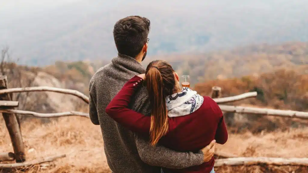 A couple standing close together and looking out over a scenic, misty landscape.