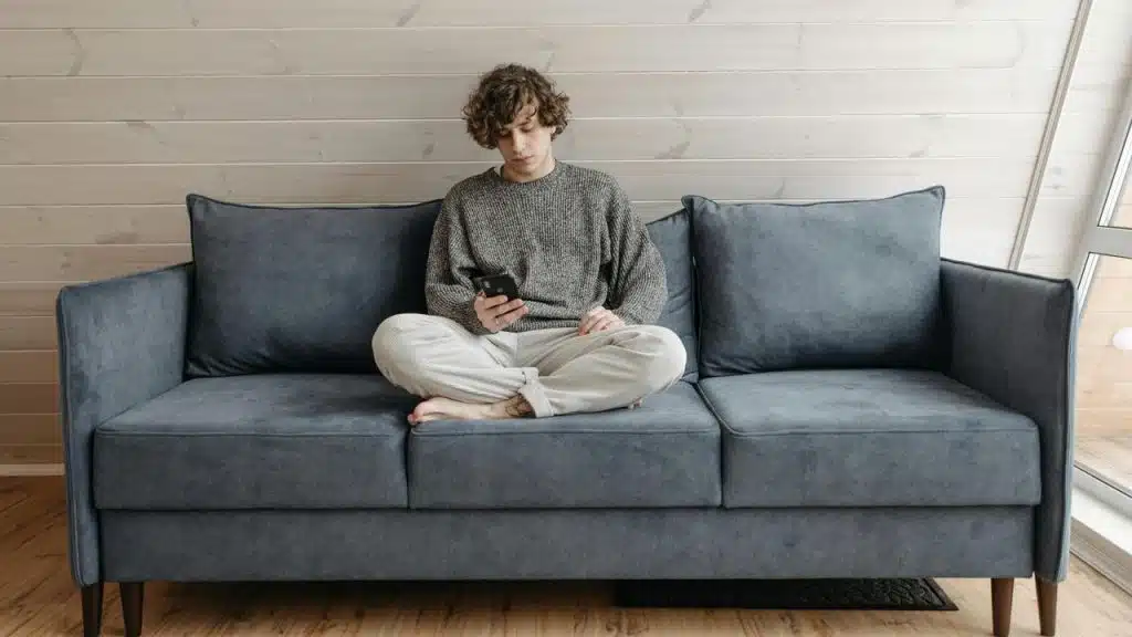 A person sitting cross-legged on a couch looking at their phone.