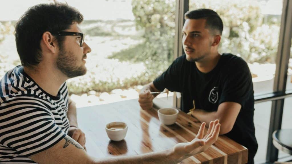 Two men sitting across a table, one in a striped shirt gesturing while talking.
