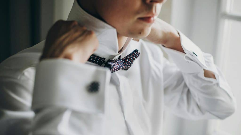 A person adjusting a bow tie on a white dress shirt.