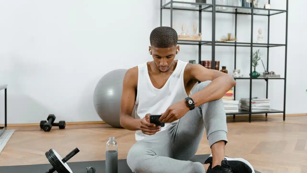 A man sitting on a yoga mat checking his phone after a workout.