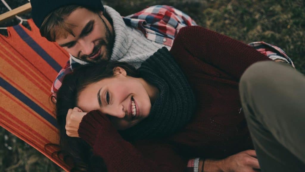 A man and woman lie in a colorful hammock, smiling and looking at one another.