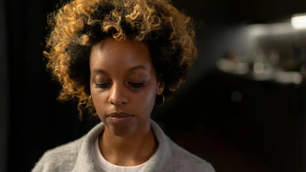 A woman with curly hair looking down in a dimly lit indoor setting.