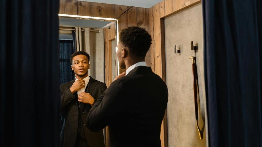 A man adjusting his tie while looking at his reflection in a mirror.