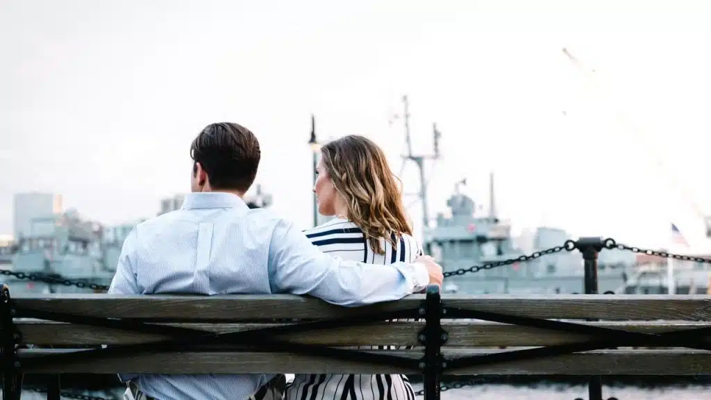 A couple sitting on a bench overlooking a harbor.