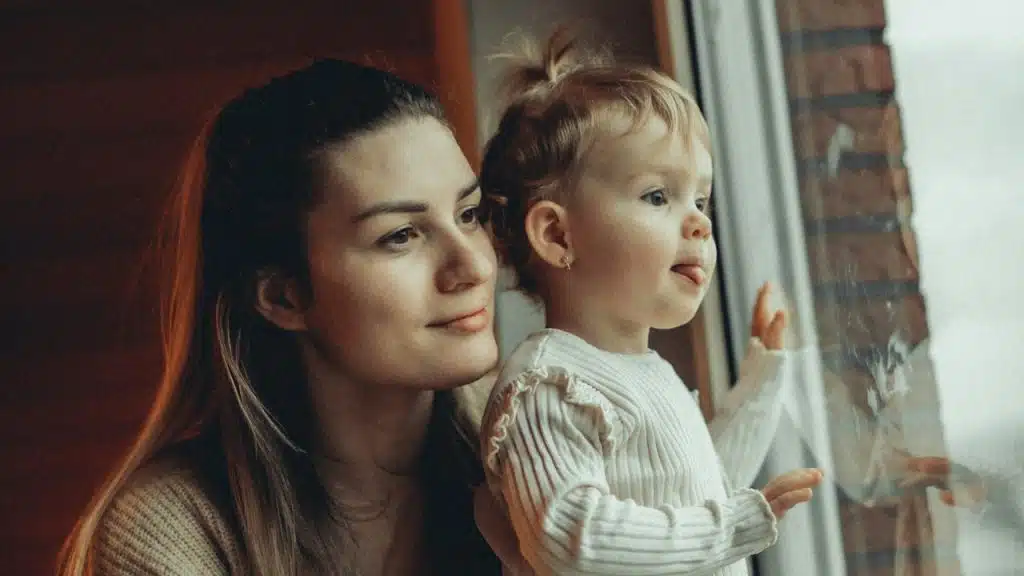 A woman holding a child looking out a window.