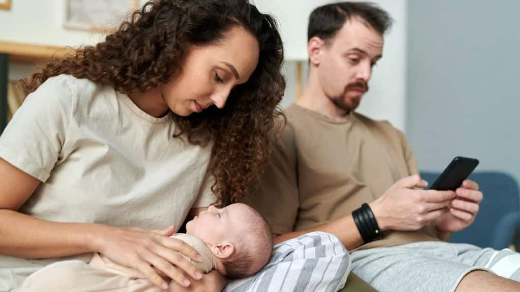 Woman tending to a baby while a man next to her looks at his phone.