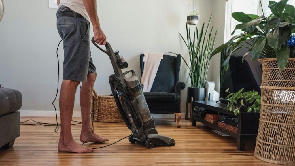 Man vacuuming a hardwood floor in a living room.