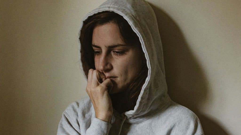 A woman sitting on a bed with a hoodie on.