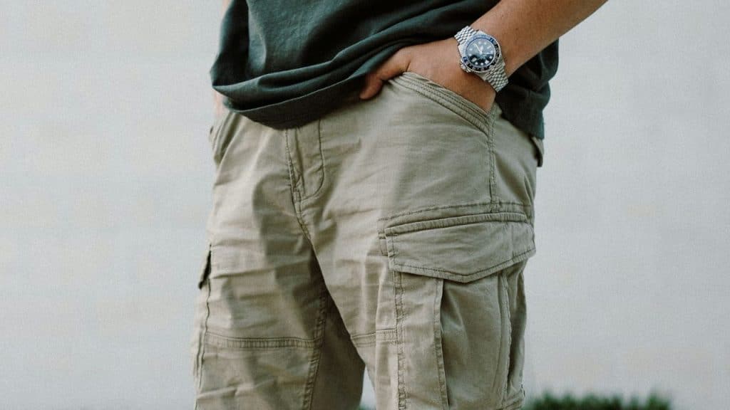 Close-up of a person wearing khaki cargo shorts, a dark shirt, and a stainless steel watch.
