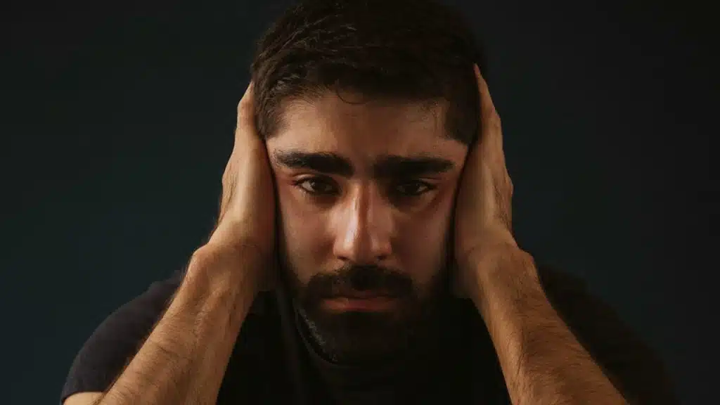 A bearded man covering his ears with his hands.