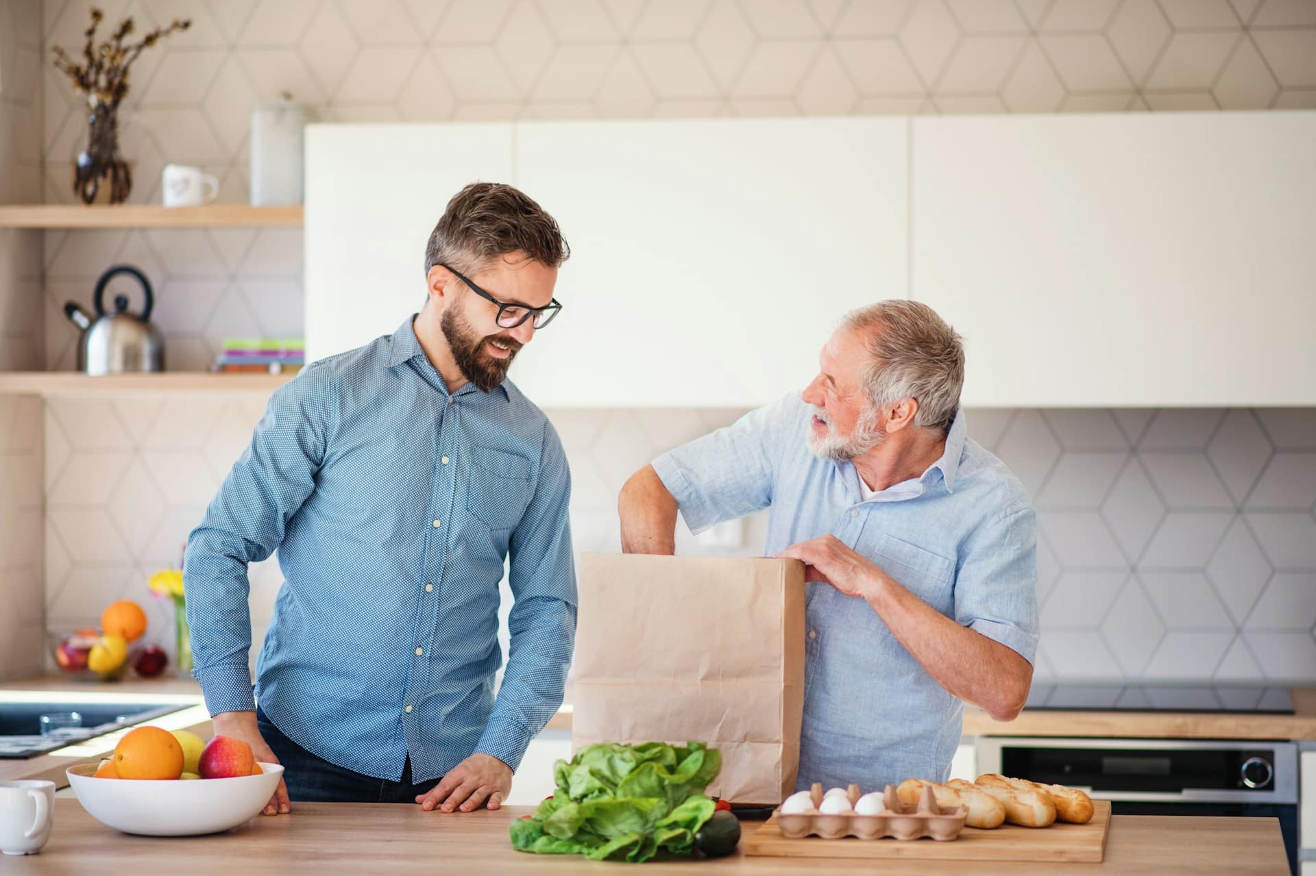 An adult man unpacking shopping bag with his father at the kitchen.