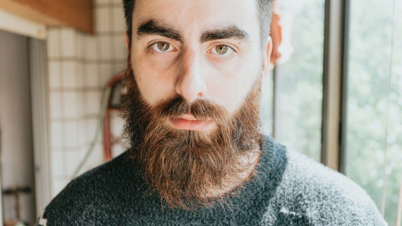 Close-up of a serious man with a full beard and prominent eyebrows, looking directly ahead.
