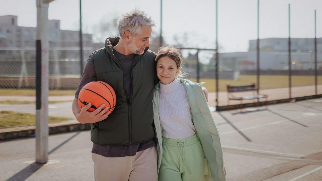 Grey-haired man and young girl smiling, walking on a basketball court.