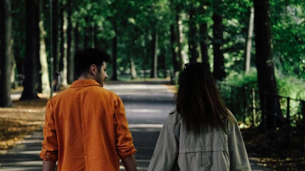 A couple walking hand in hand down a tree-lined path.