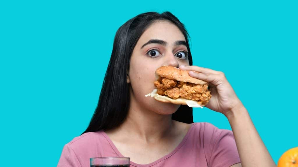 A young woman wearing a pink T-shirt is eating a burger.