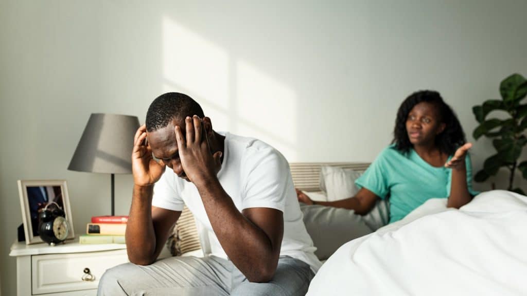 A woman screaming on her husband, who is sitting with her on the bed.