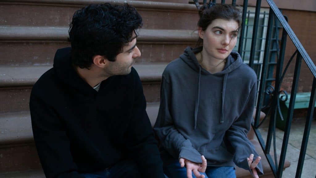 A man and a woman sitting on brown stone steps outside, engaged in a conversation.