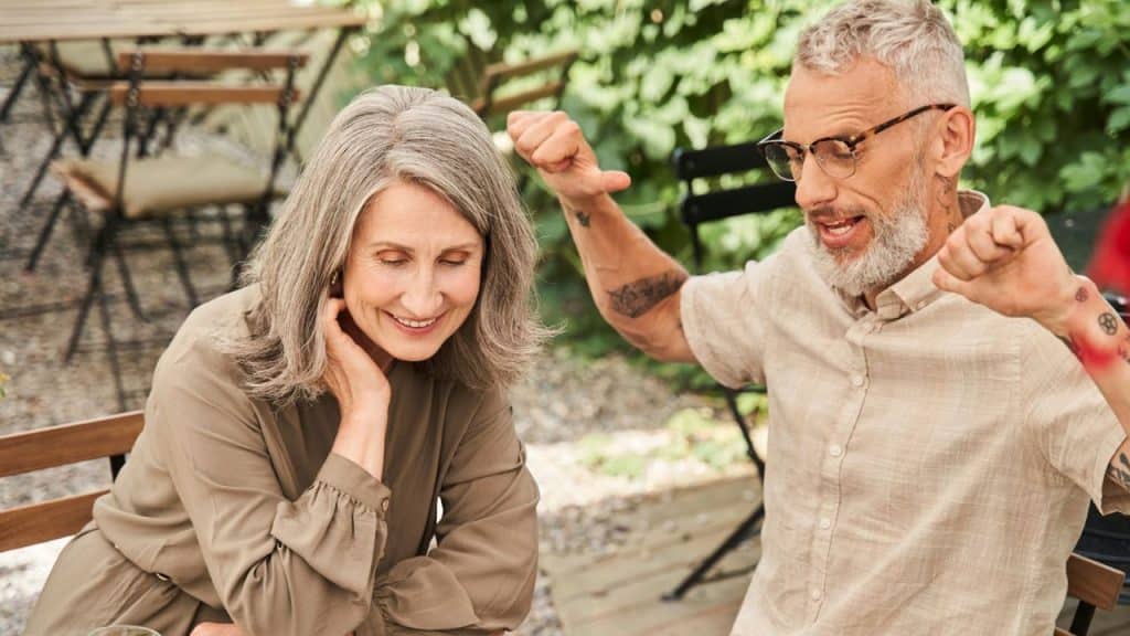 Older couple sitting at an outdoor table, woman smiling while man gestures excitedly.
