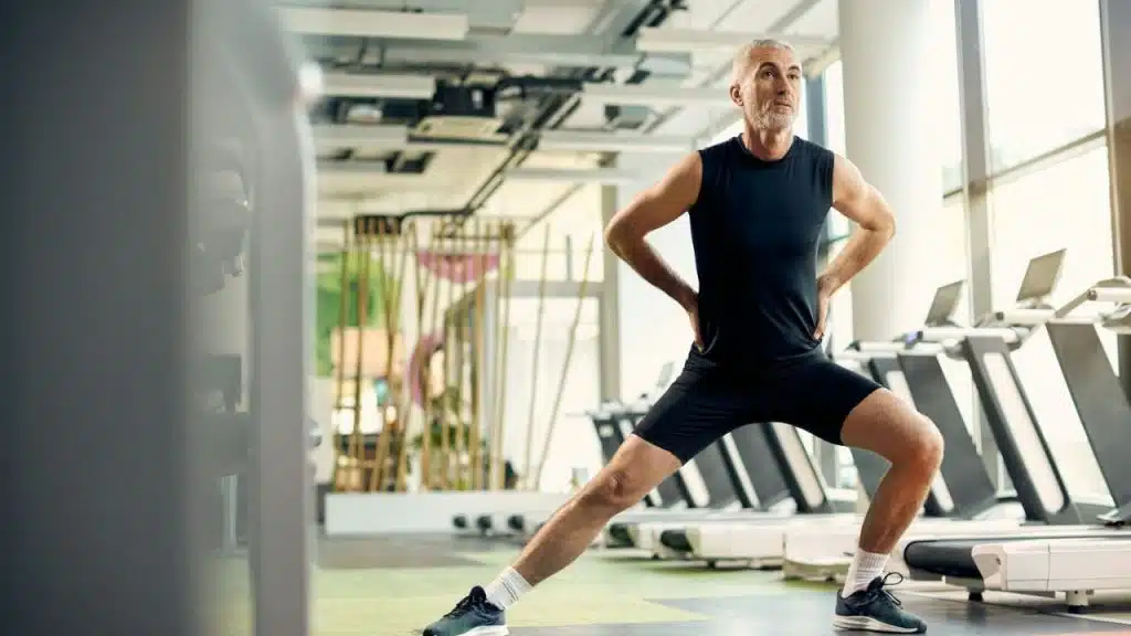 A middle-aged man does a lunge exercise in a modern, bright gym.