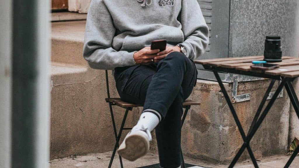 A person sitting on a chair outdoors while looking at their phone.