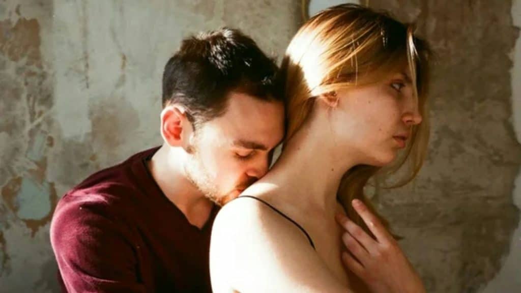 Man kissing woman's neck from behind; woman looks away from the camera.