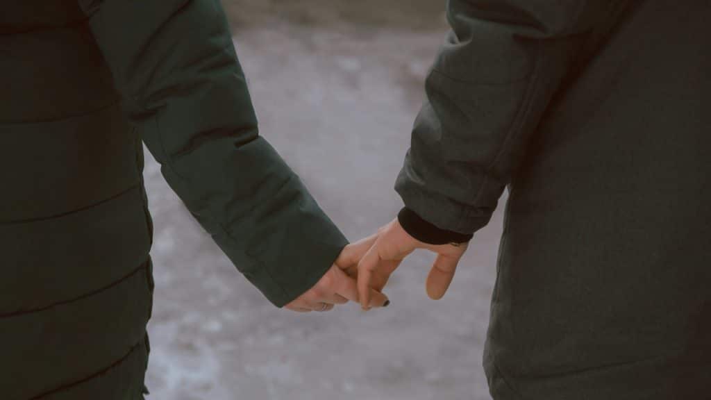 A close-up of a couple holding hands outdoors while wearing dark green winter jackets.