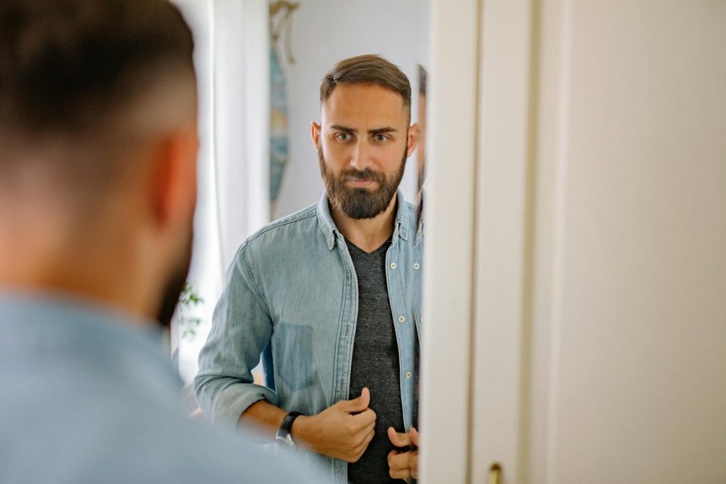A man wearing a denim jacket, looking at the mirror.