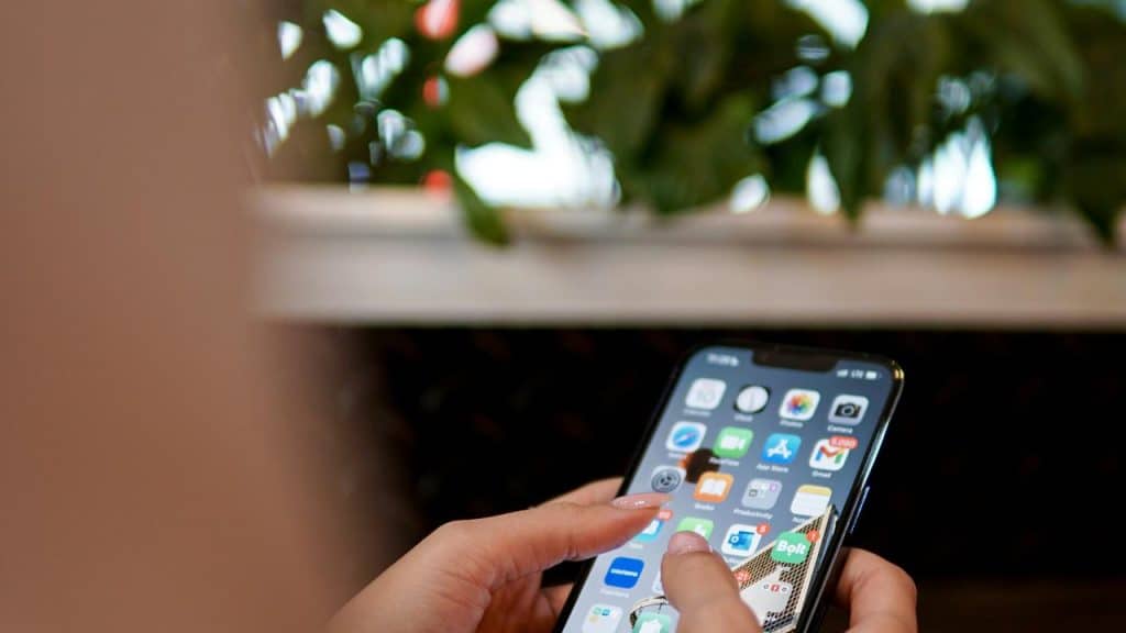 A person holding a smartphone with apps displayed on the screen.