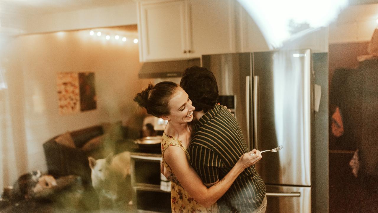 A couple hugging and laughing together in a kitchen.