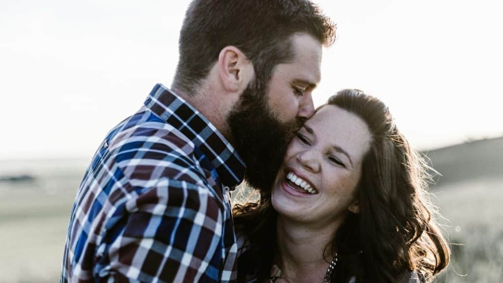 A bearded kissing a smiling woman on the cheek.