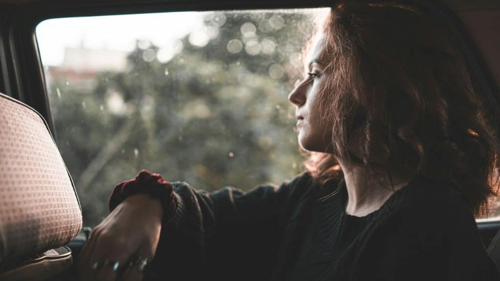 Profile of a woman with red hair looking out a car window on a sunny day.