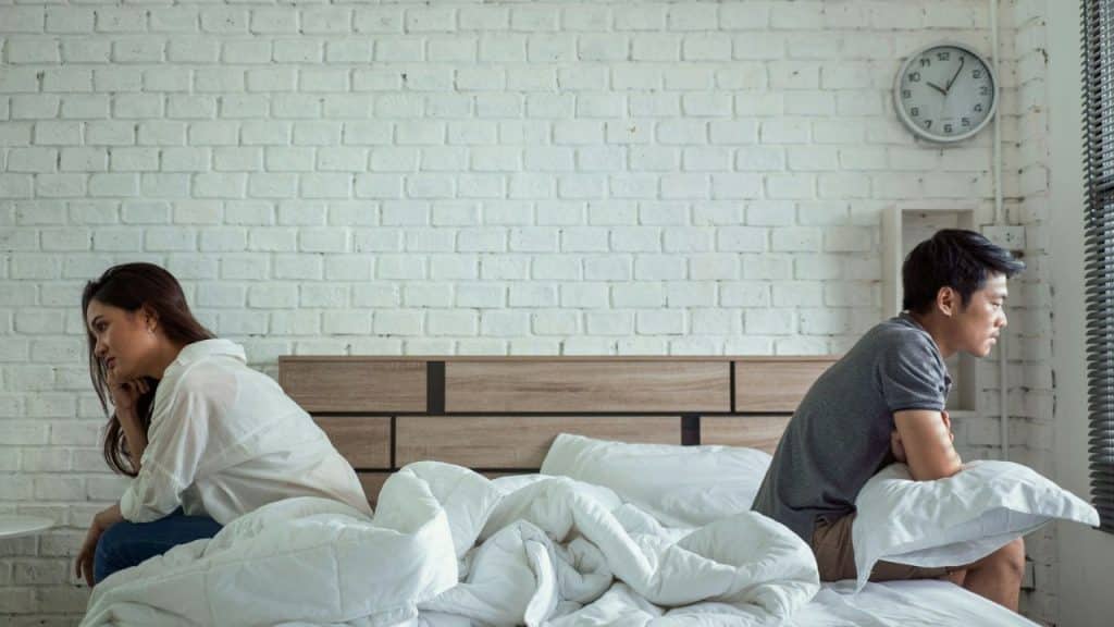A man and woman sit facing away from each other on opposite sides of a bed.
