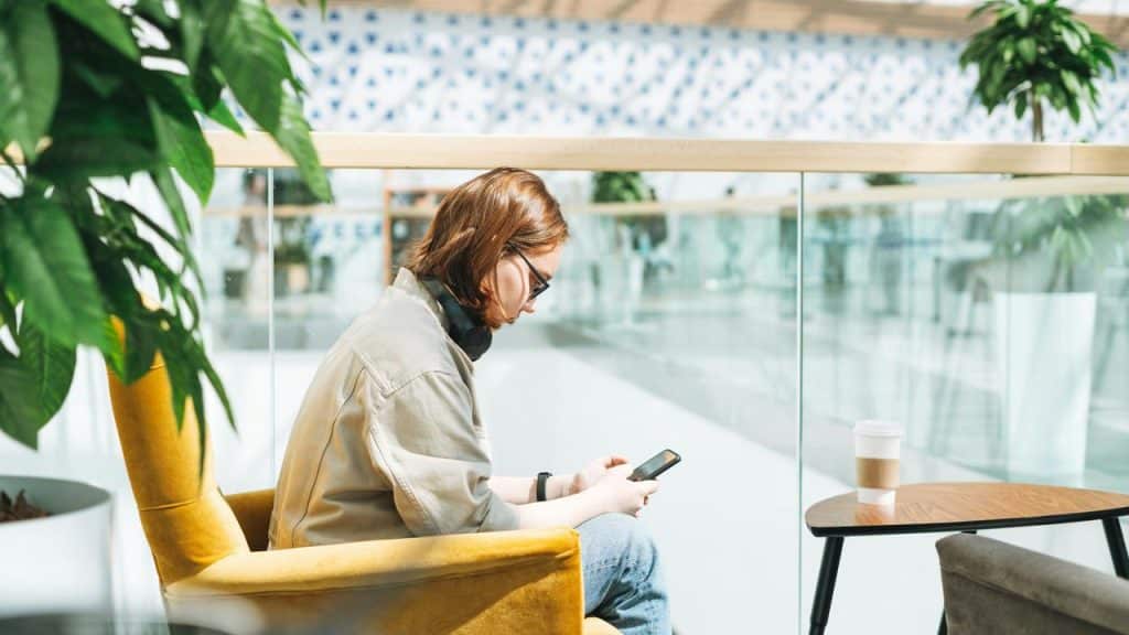 A person sitting outside with a smartphone and coffee.