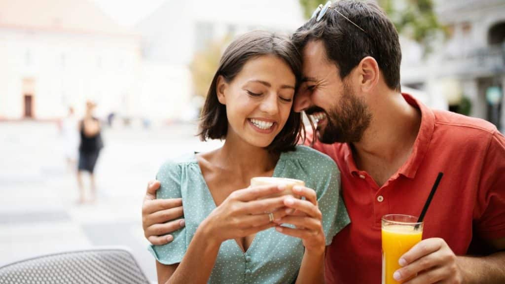 Smiling couple at an outdoor cafe, woman holding a cup, man with orange juice.