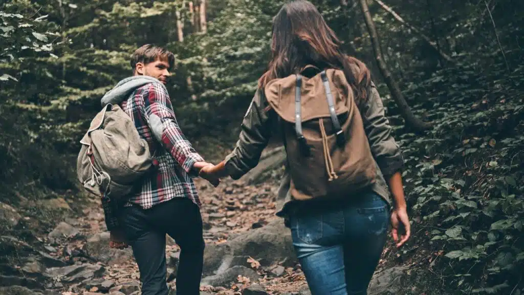 Couple hiking, holding hands on a rocky path; man looks back.