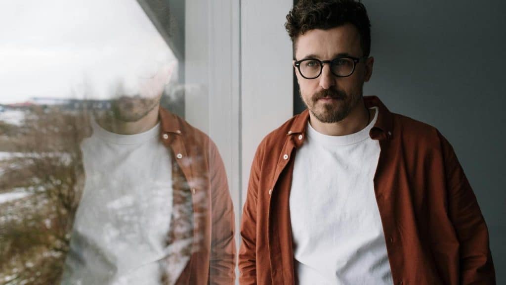A man wearing glasses standing by a window.