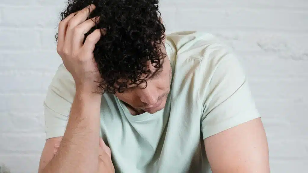 A man sitting with his head down and hand on his hair looking upset.