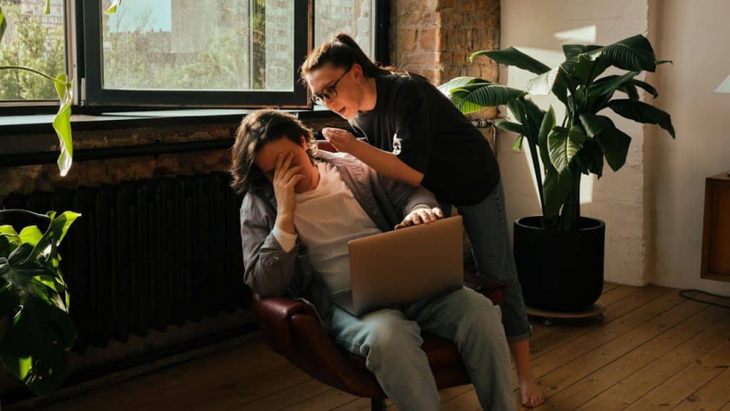 A woman getting angry at her husband, who is working on a laptop.