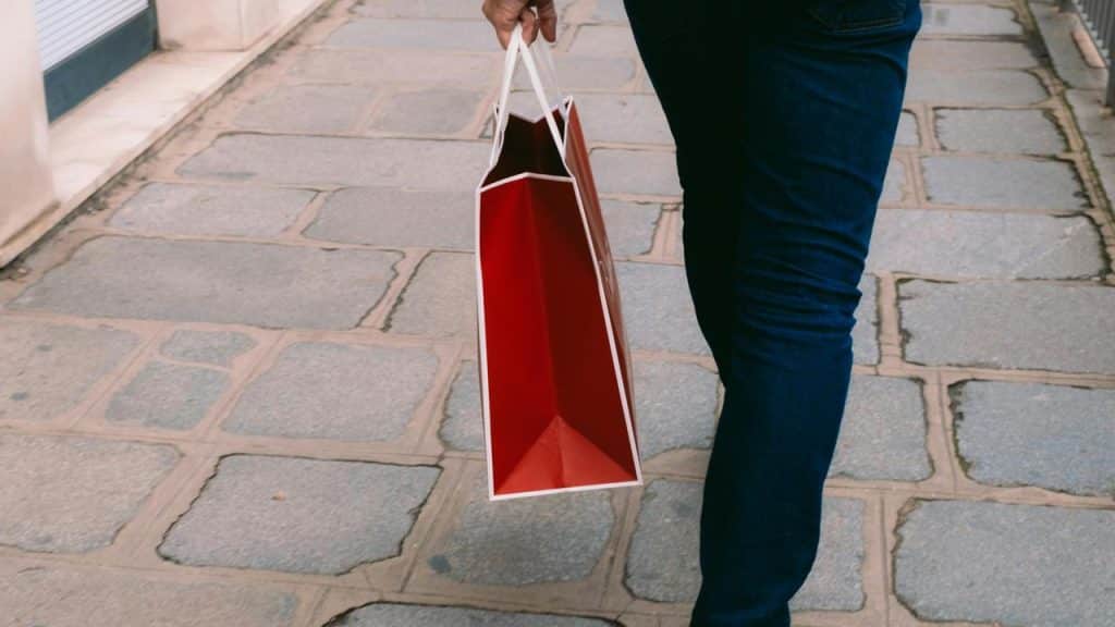 A person carries a red shopping bag on a sidewalk.
