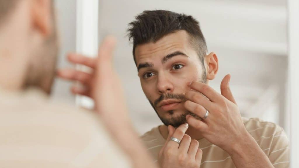 Man in a striped shirt looking at his reflection while touching his face.