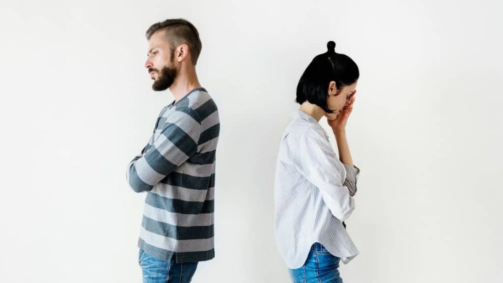 Man and woman standing back-to-back against a white wall in separate distress.