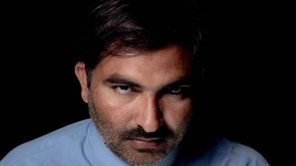Close-up of a middle-aged man's face, partially shadowed, looking intently at the viewer.